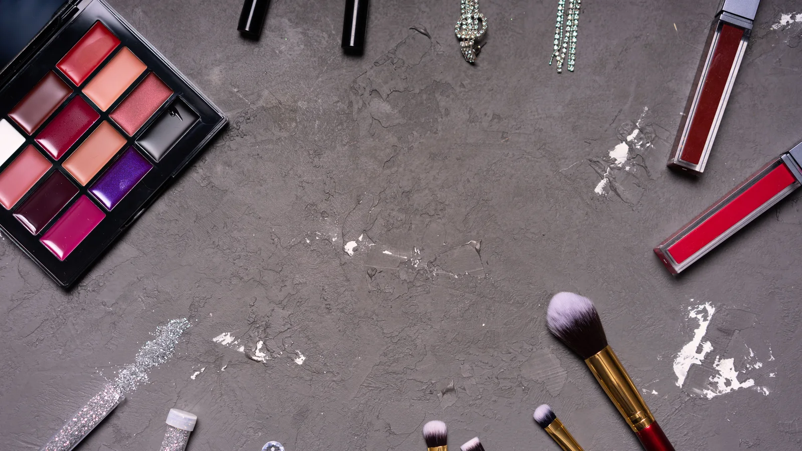 Colour palettes, brushes and scattered cosmetic powder on a grey surface.