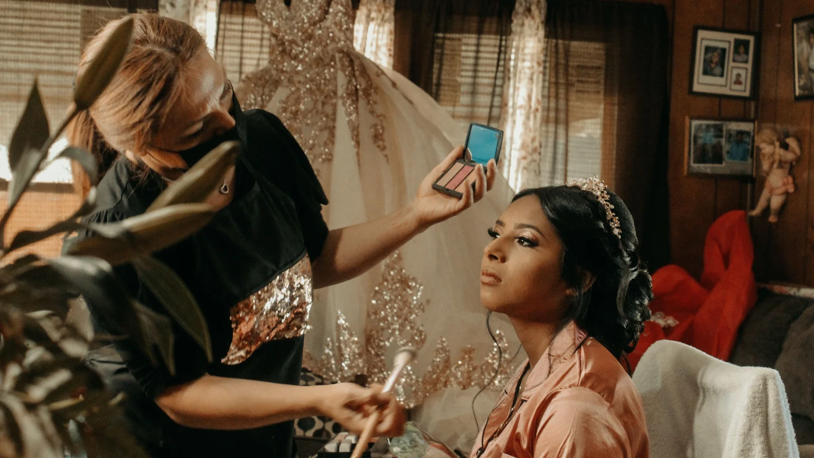 A make-up artist applying cosmetics to a seated woman in a peach robe.