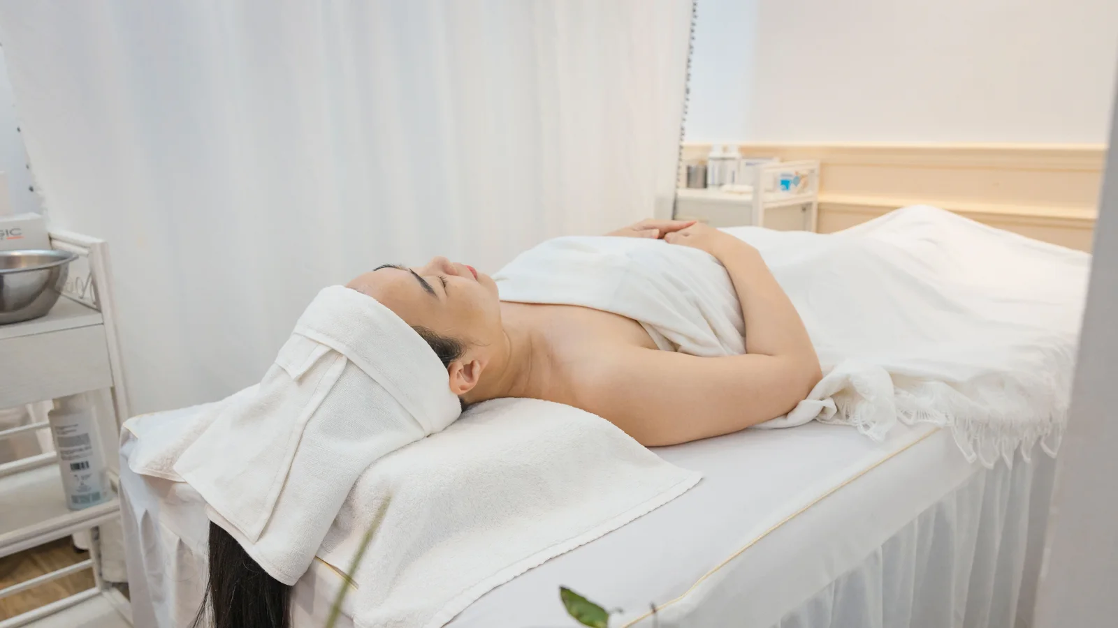 A woman resting on a treatment bed beneath pale towels.