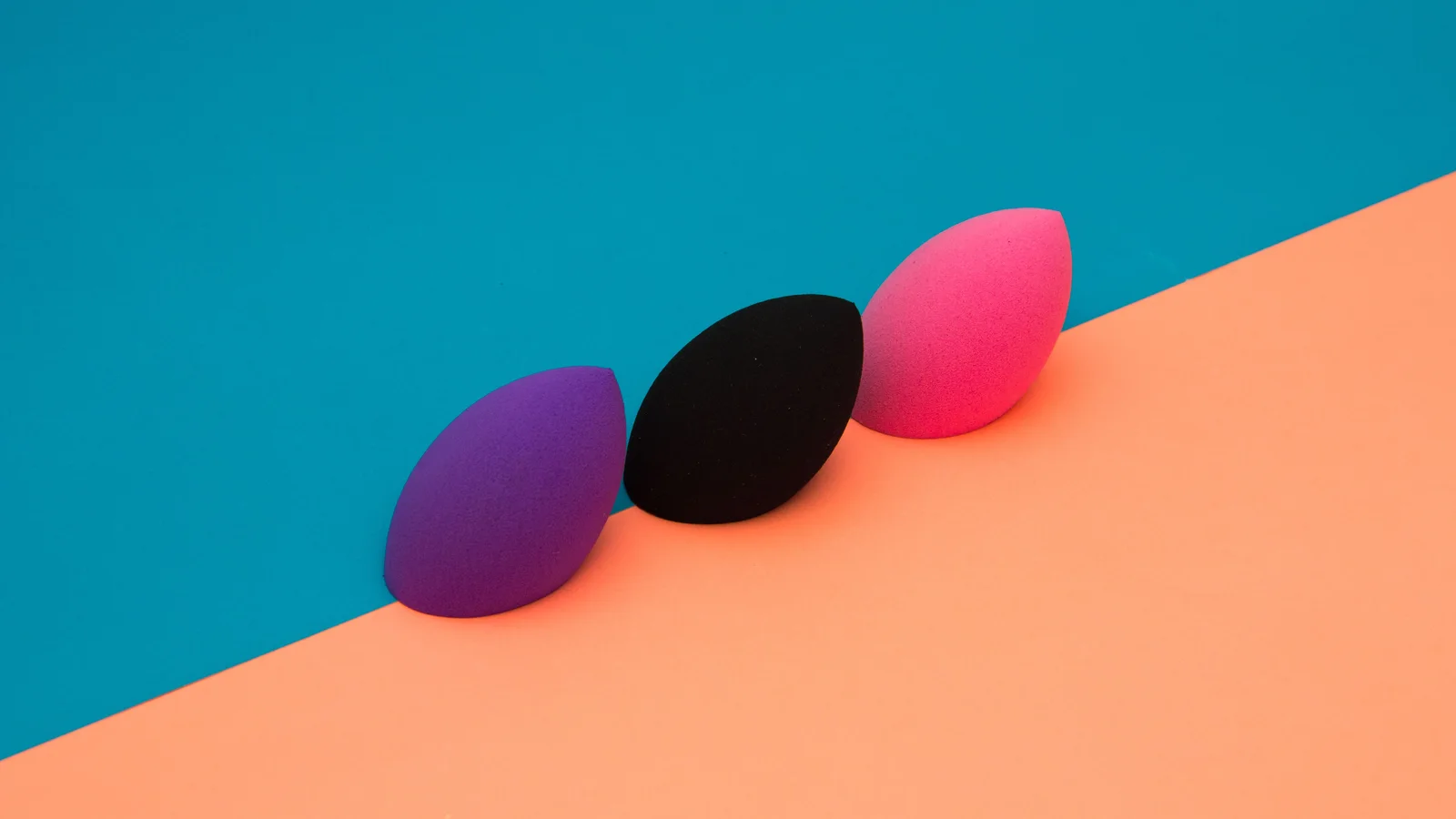 Purple, black and pink make-up blending sponges on an orange and turquoise background.