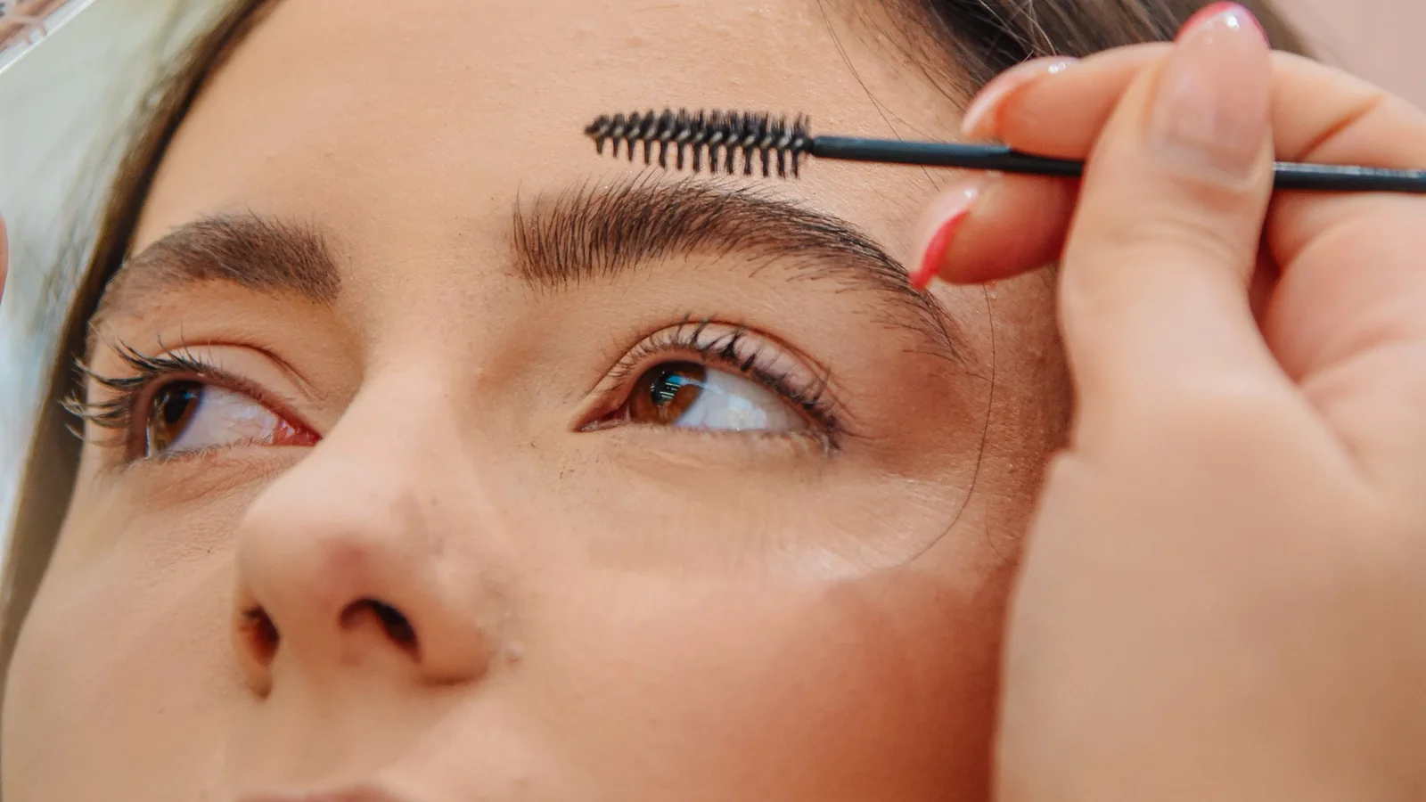 A woman brushing her eyebrow upwards with a small spoolie.