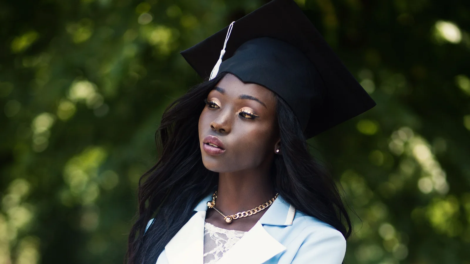 A woman wearing a graduation cap and a pale belted outfit outdoors.