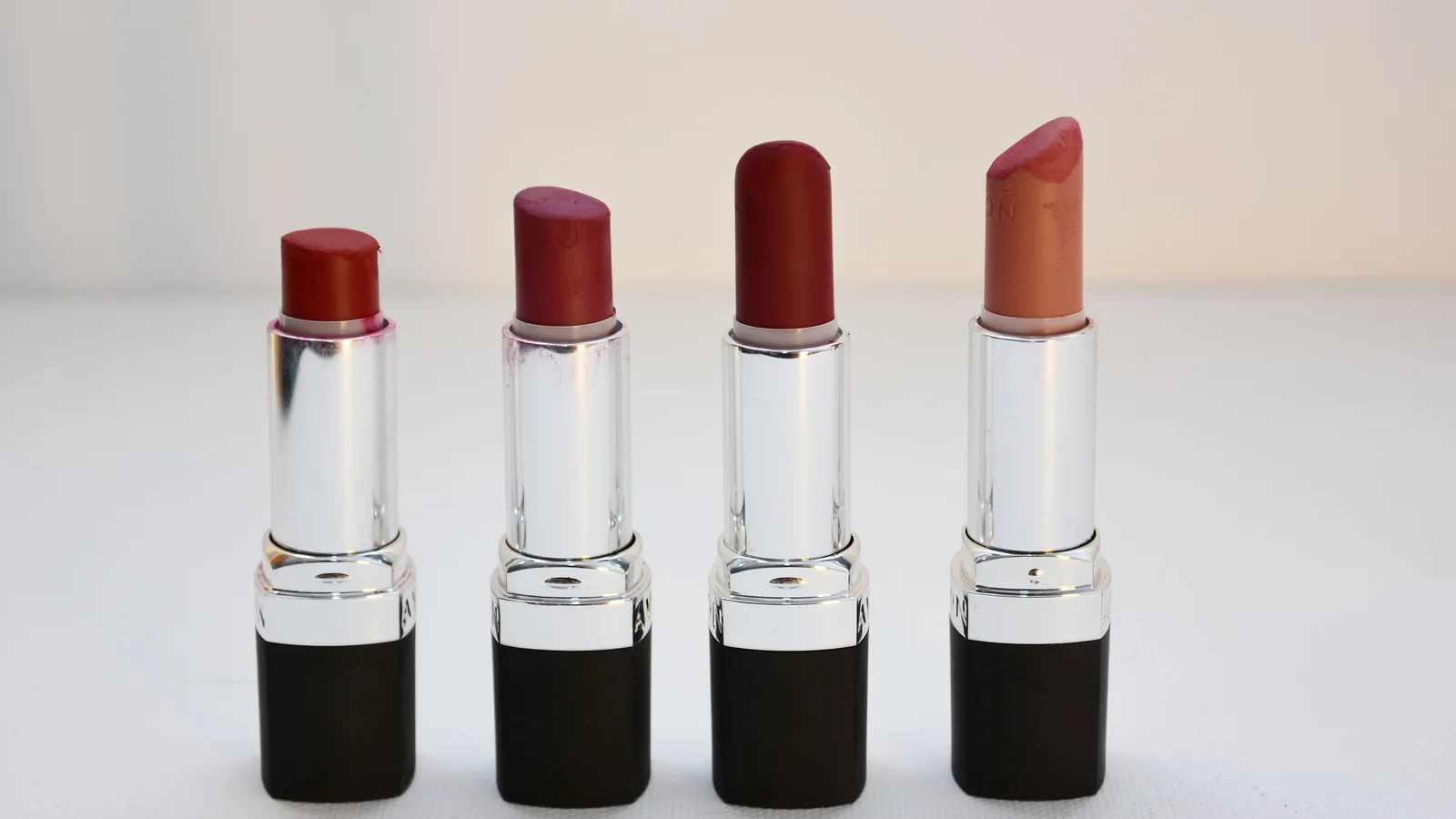 Four open lipsticks in different warm and red shades.