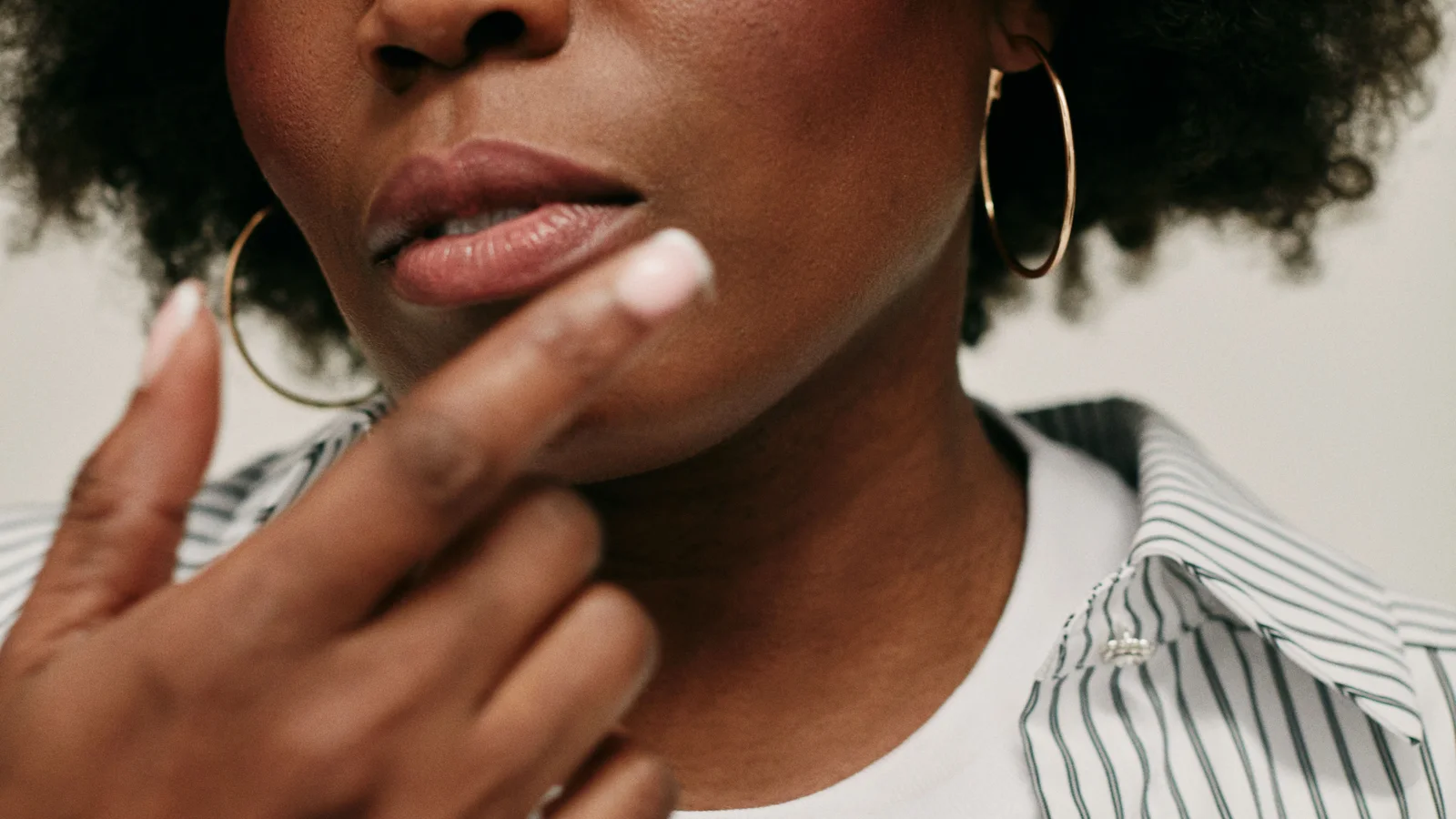 A woman touching her chin with one finger while holding a small cosmetic jar.