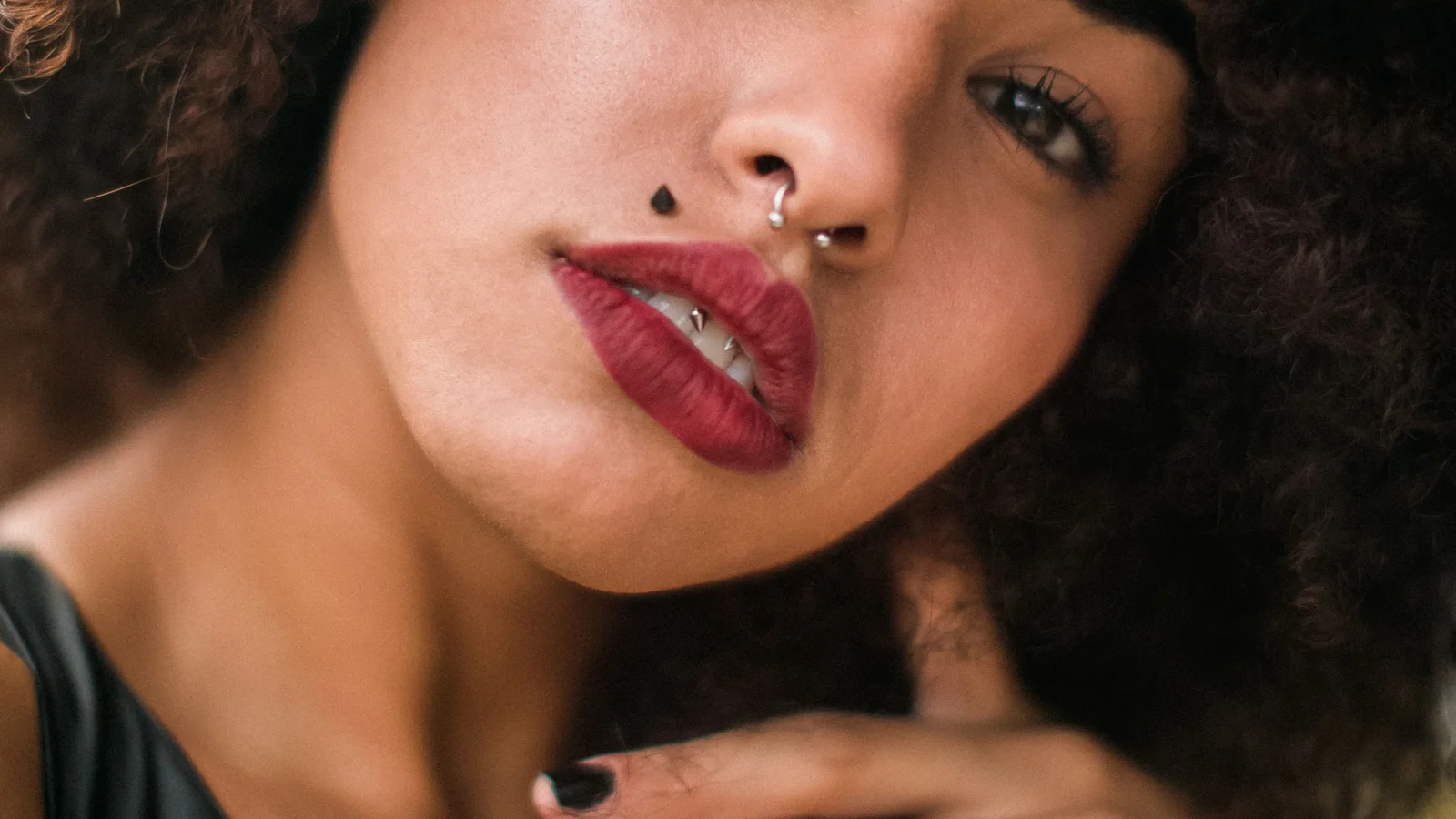 Close-up portrait of a woman with curly hair, a nose ring and softly coloured lips.