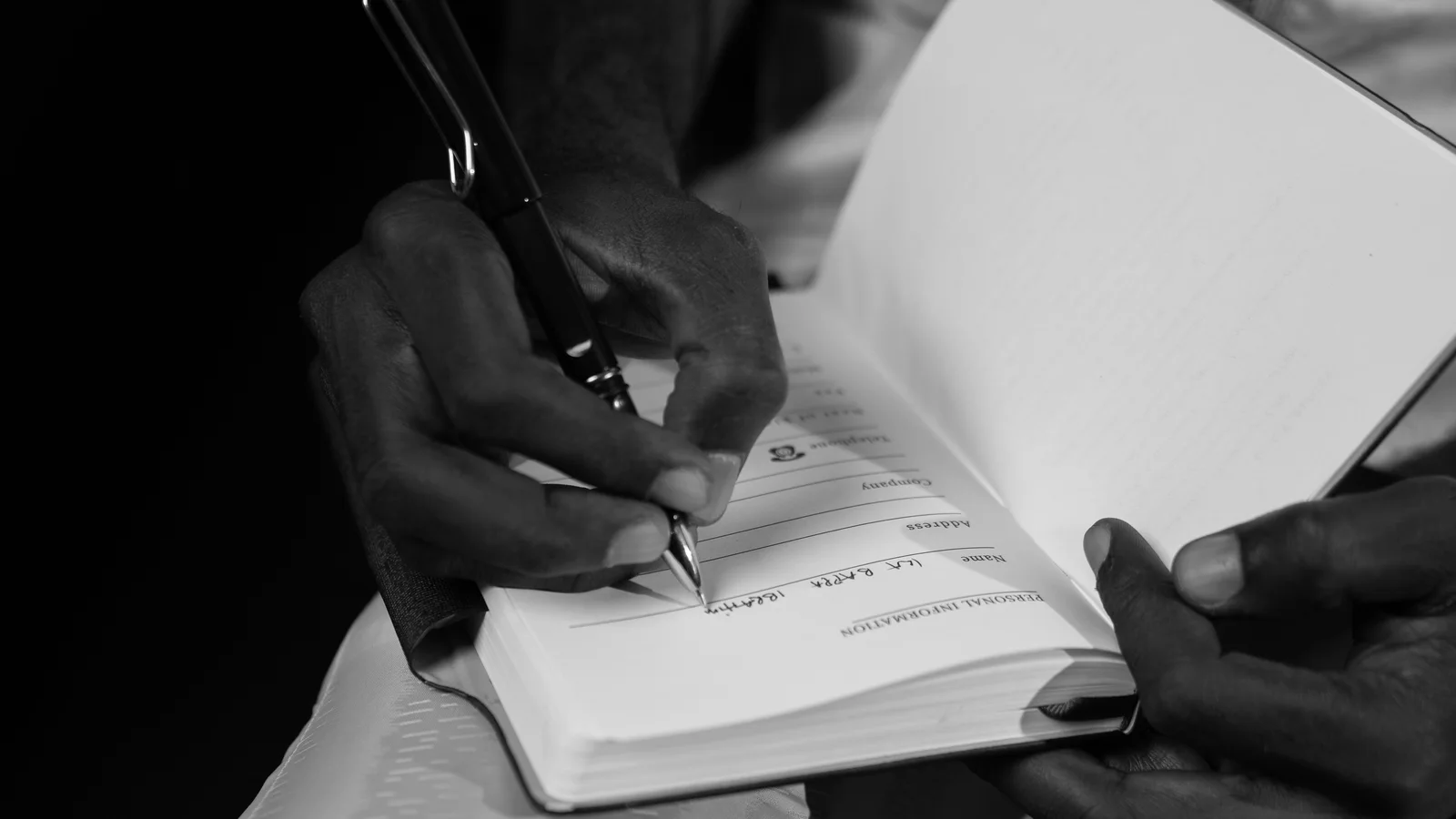 Black-and-white close-up of hands writing in a small notebook.