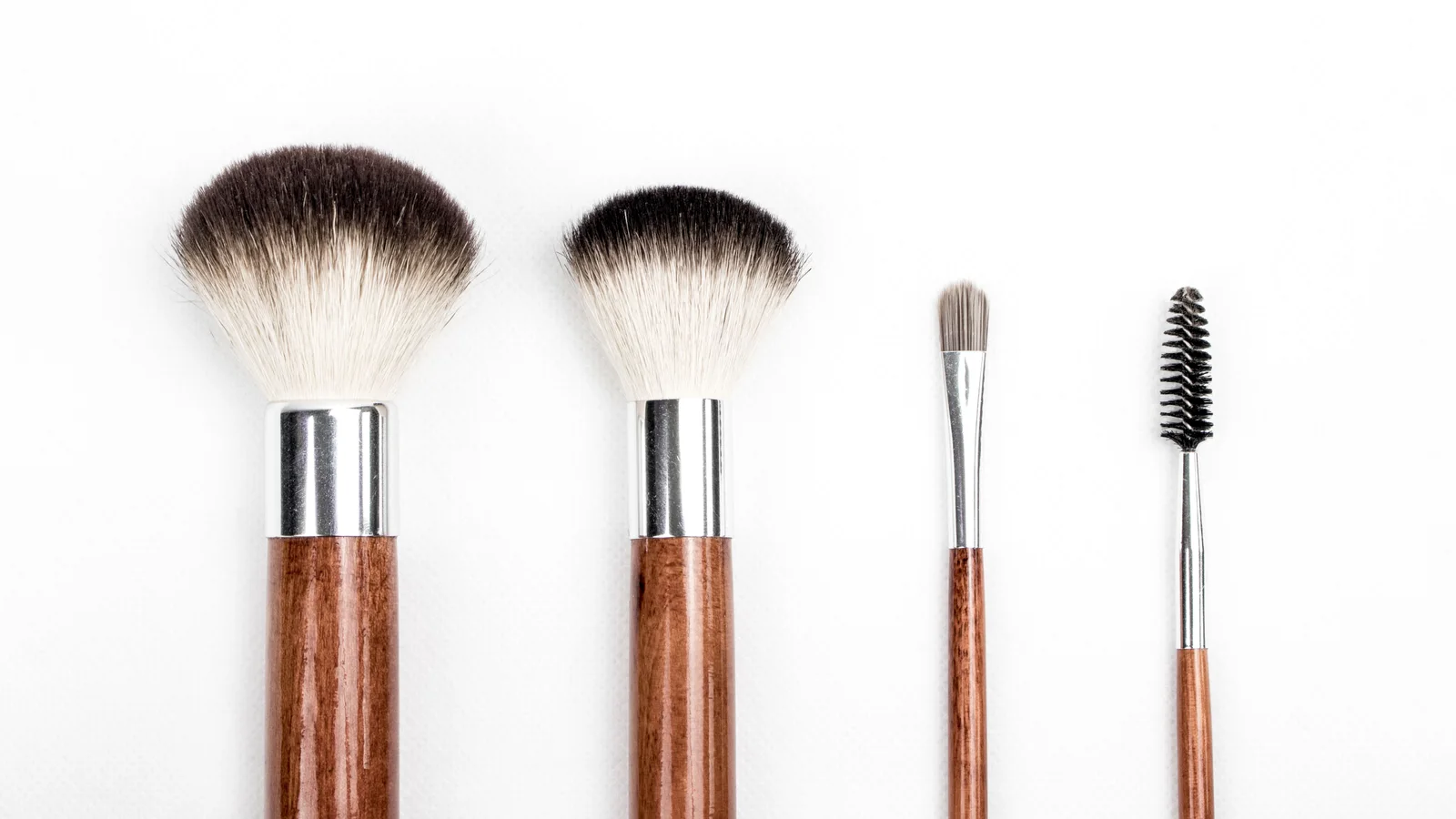 Four make-up brushes with wooden handles against a white background.