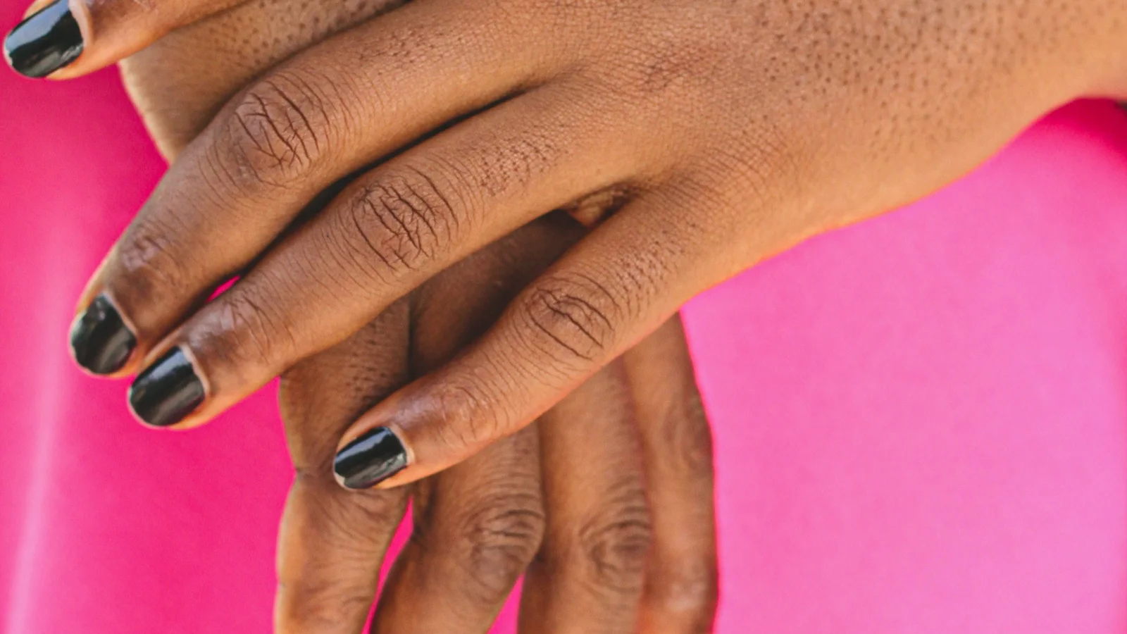 Crossed hands with dark nail polish and a silver ring.