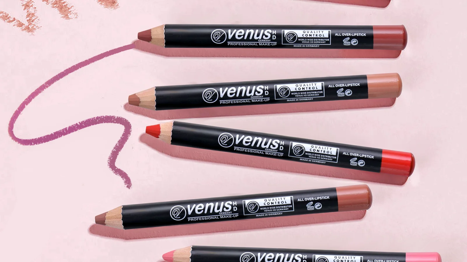 A row of coloured lip pencils and matching colour strokes on a pink surface.