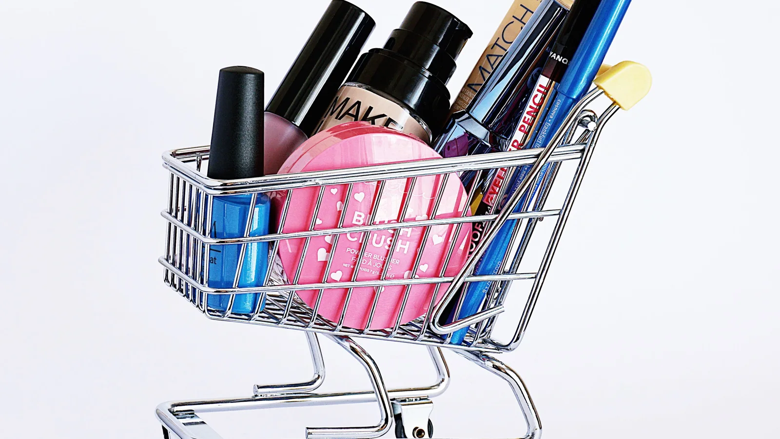 A miniature shopping trolley filled with cosmetic tubes and pencils.