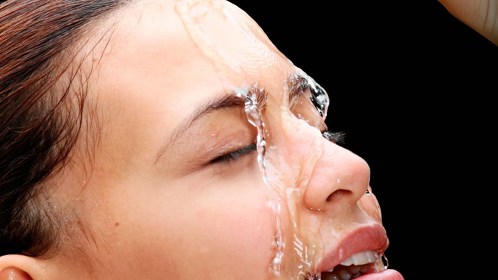 A woman pouring water from a glass onto her face.