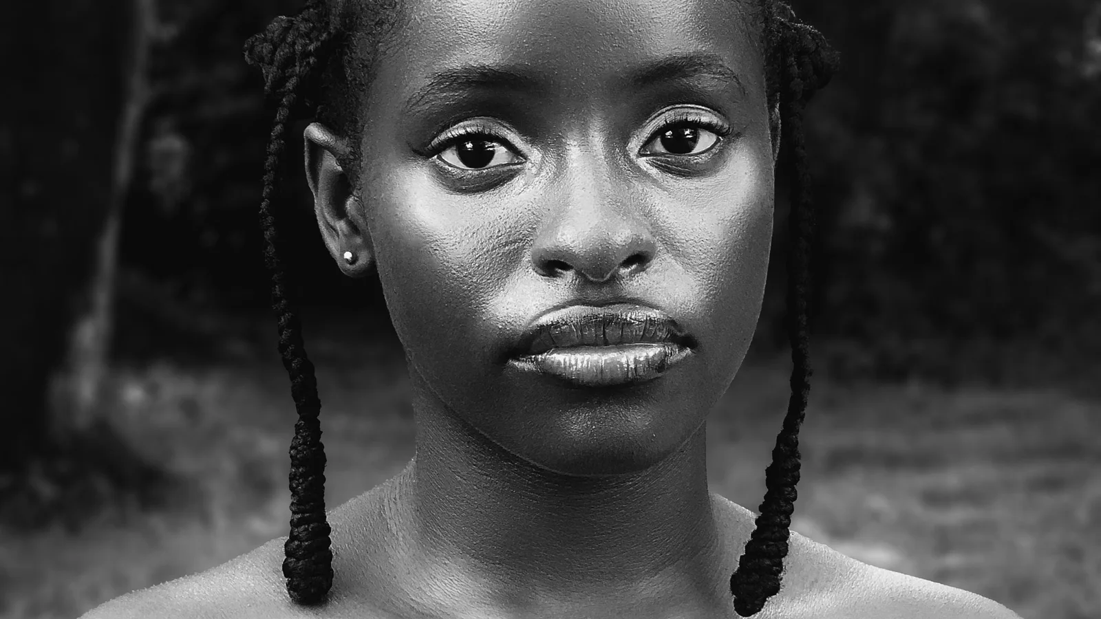 Black-and-white portrait of a woman with braided hair looking towards the camera.