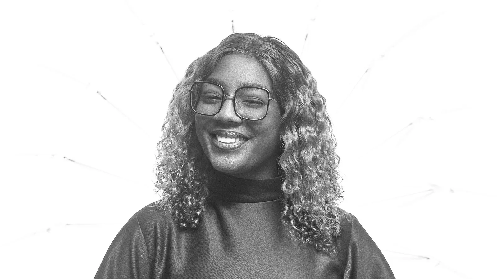 Black-and-white portrait of a smiling woman wearing glasses and a dark dress.