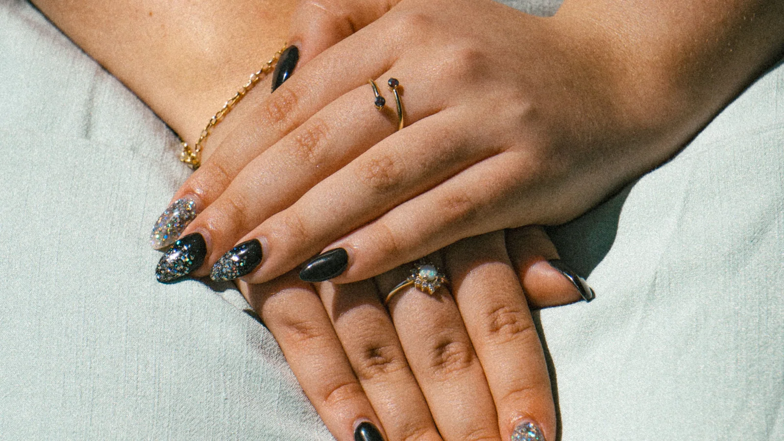 Hands with black and silver nail decoration resting together.