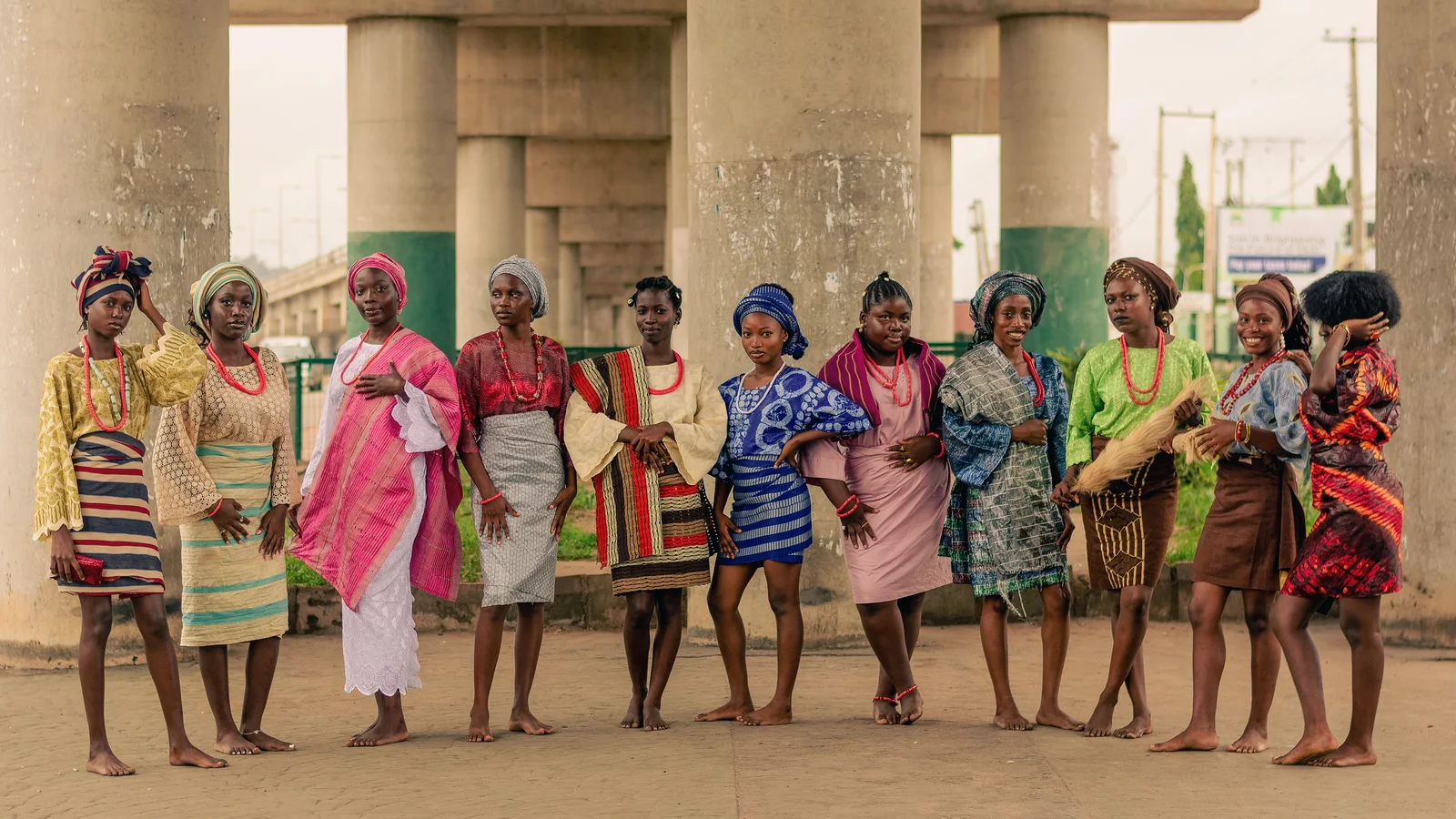 A row of women wearing colourful dresses beneath a concrete structure.