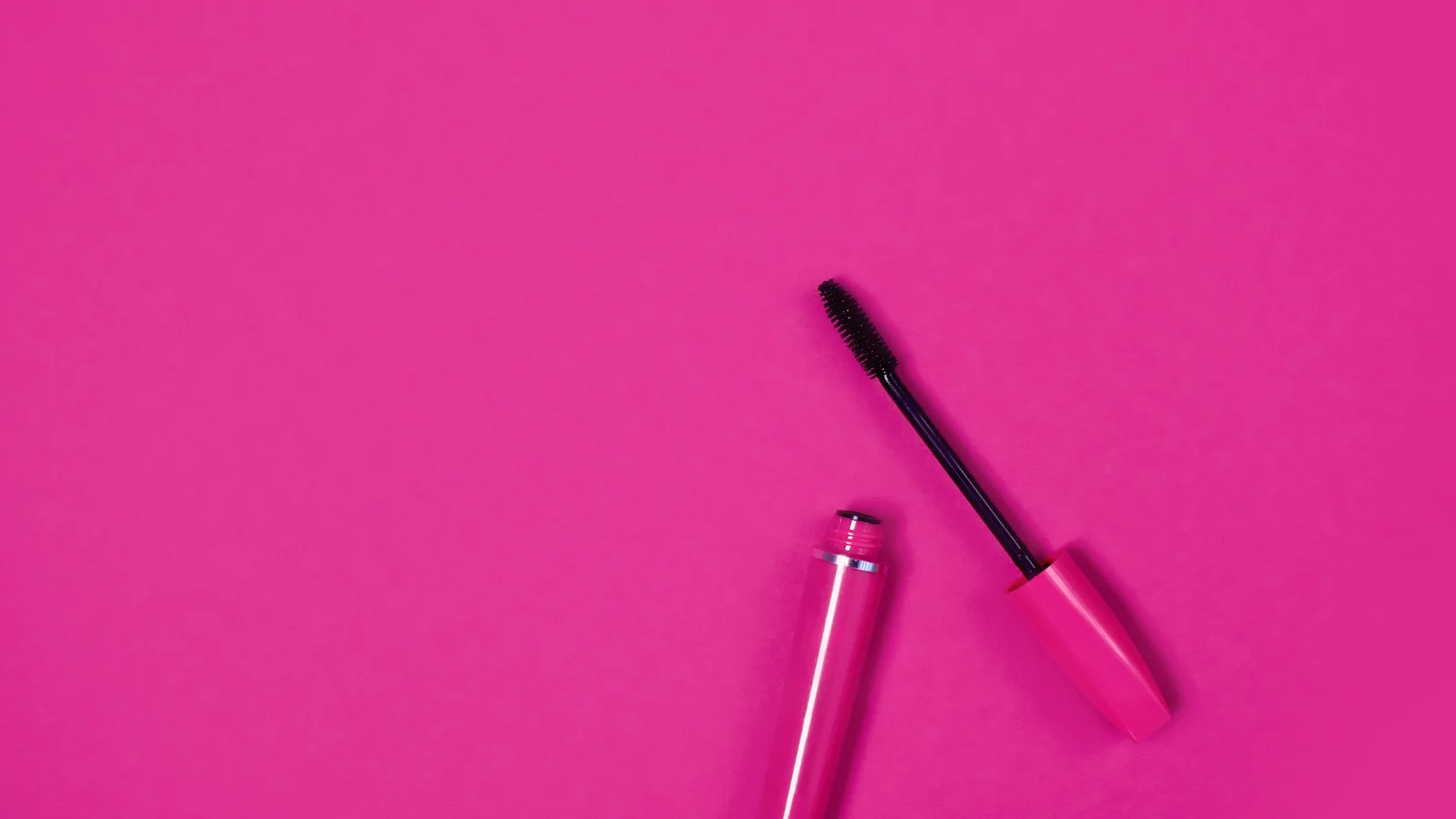 An open mascara tube and wand on a pink background.