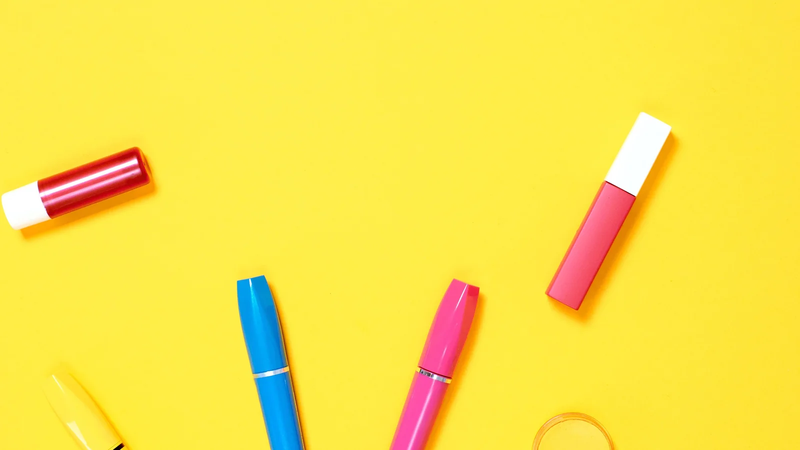 Cosmetics and a small tan pouch arranged on a bright yellow background.