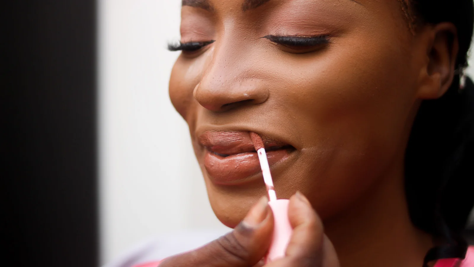 A woman applying a muted pink lip gloss with a wand.