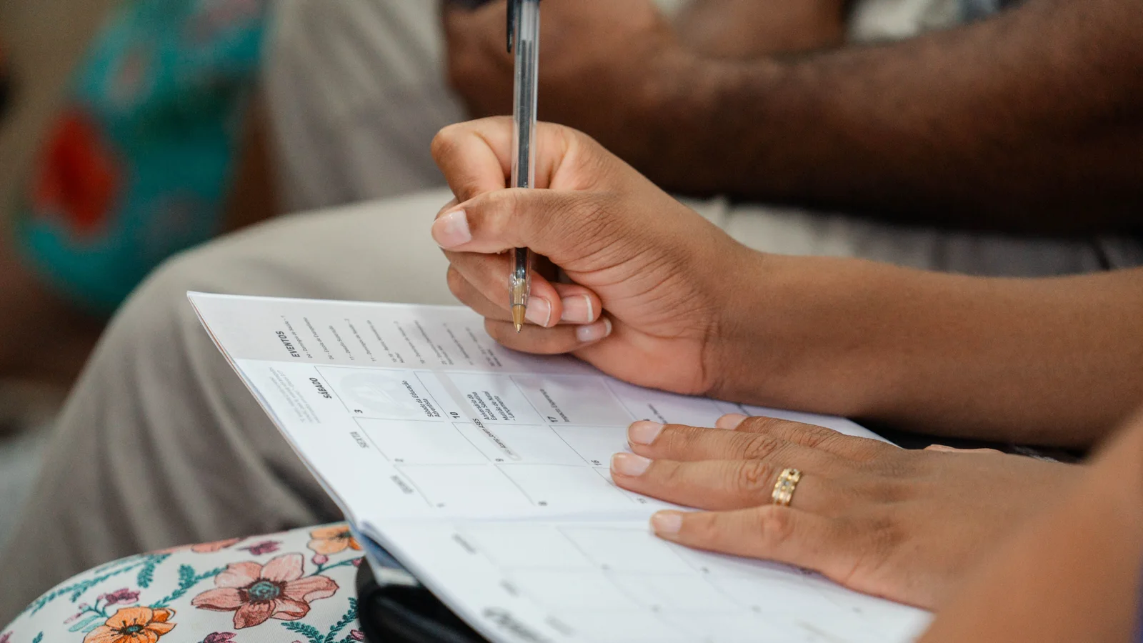 A person writing in a calendar planner while seated beside another person.