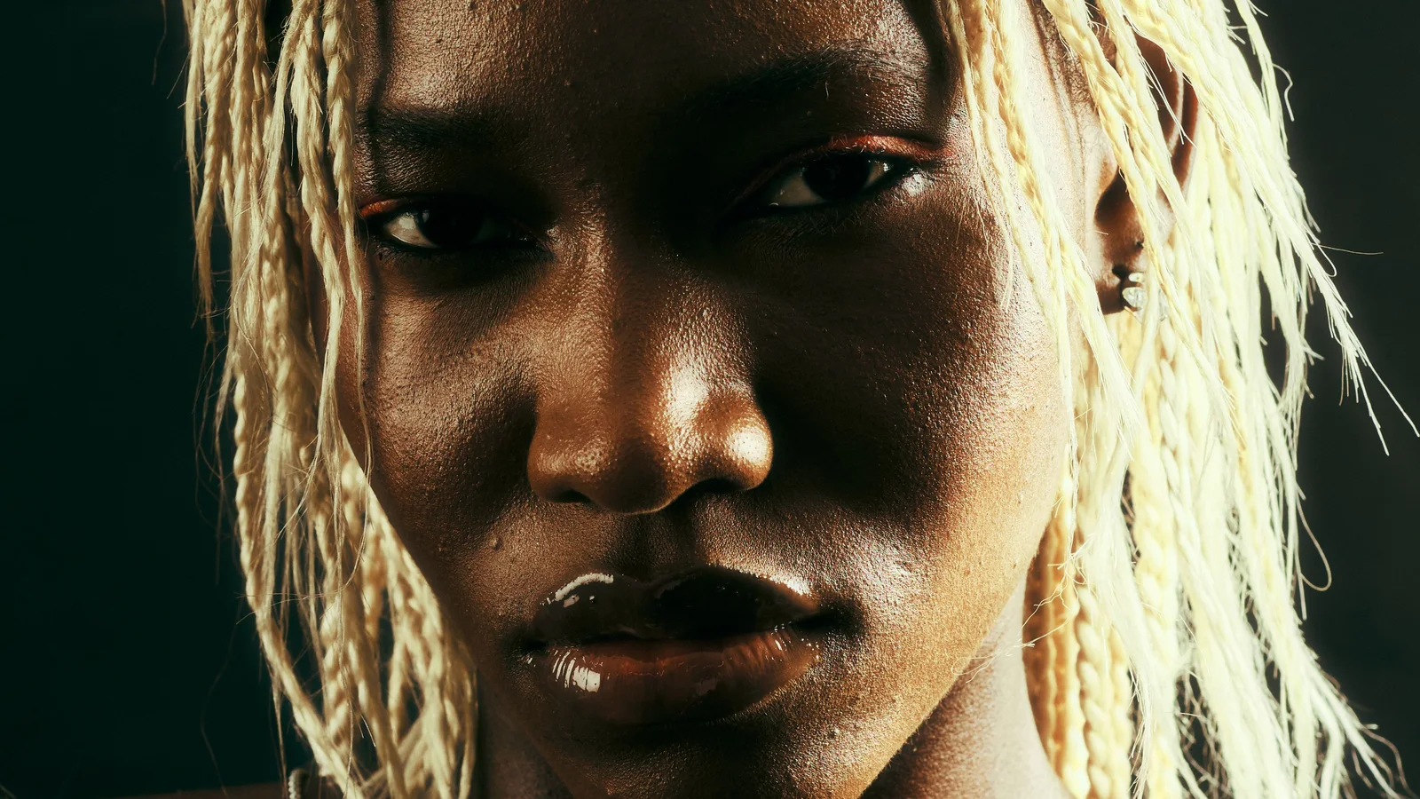 Portrait of a woman wearing blonde braids against a dark background.