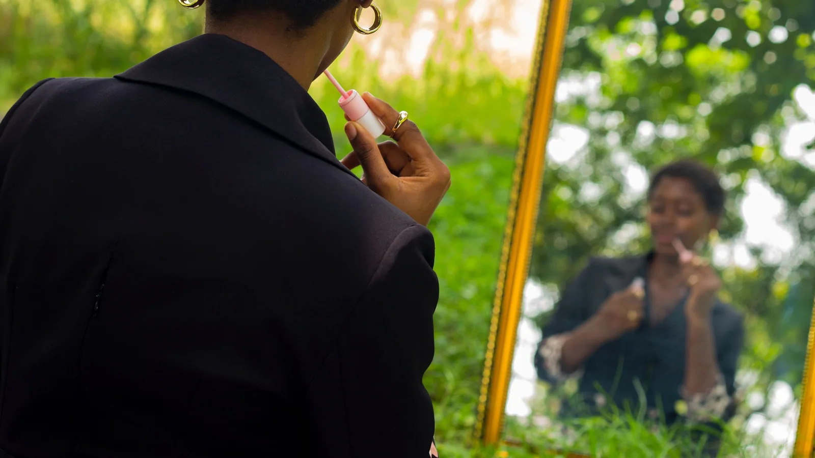 A woman applying lip colour while seated in front of a mirror outdoors.