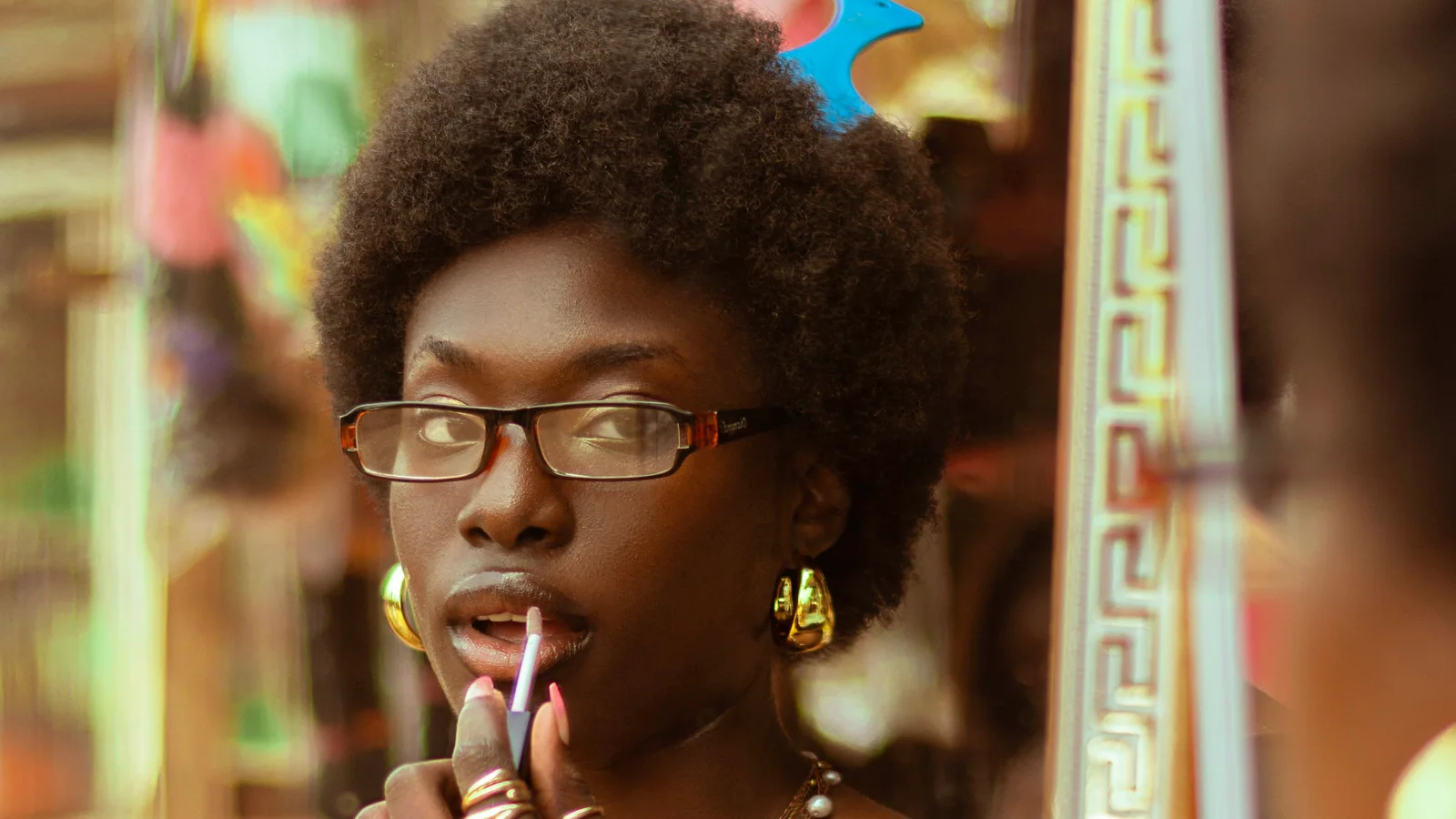 A woman wearing glasses applying lip colour in front of a mirror.