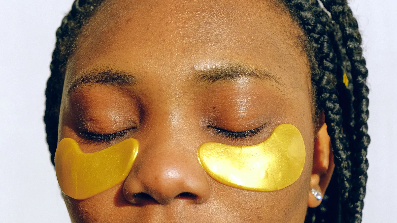 A woman with closed eyes wearing gold-coloured patches beneath her eyes.