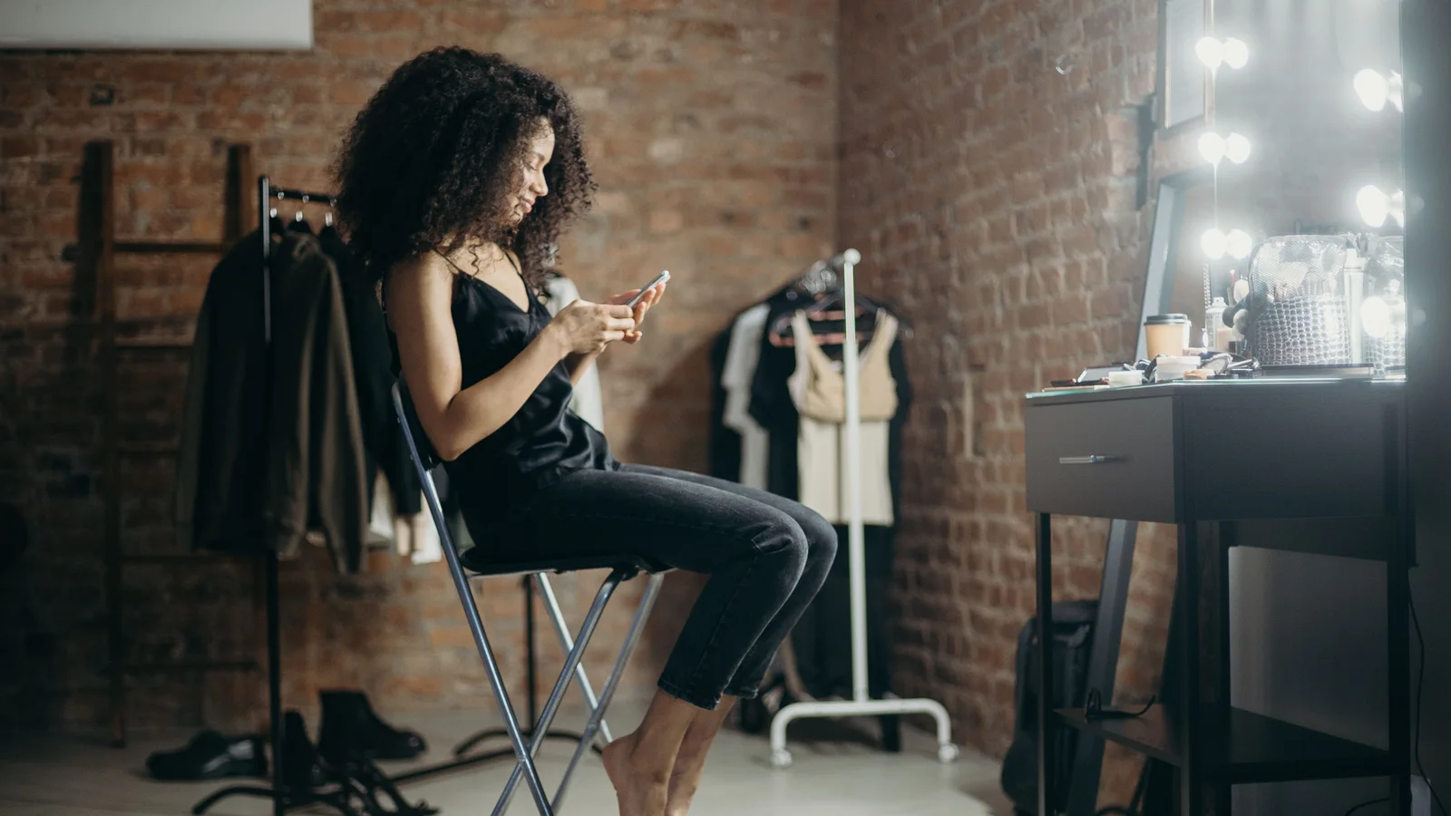 A woman seated at a dressing-room table looking at a phone.