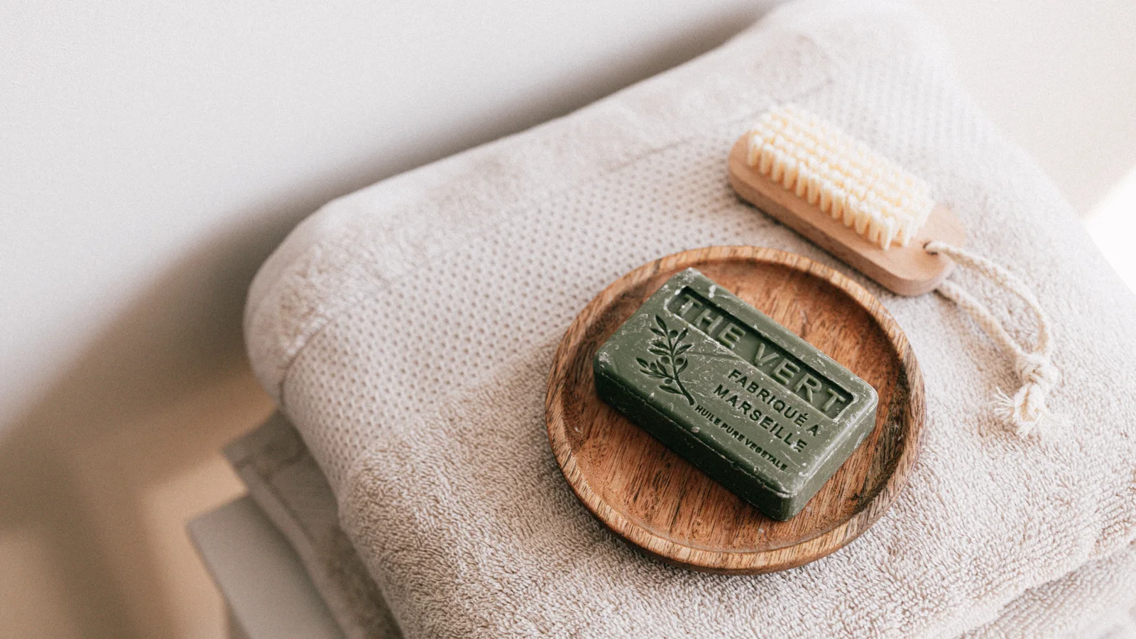 Folded towels with a bar of soap and a wooden body brush.