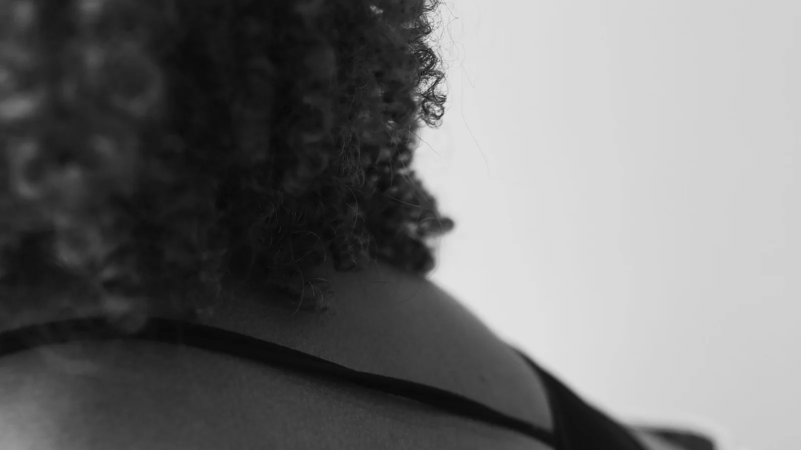 Black-and-white photograph of a woman's upper back and shoulder beside curly hair.