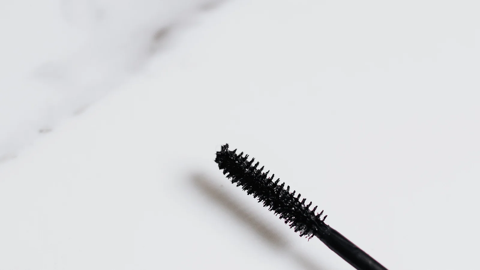 An open mascara tube and wand on a pale marble surface.