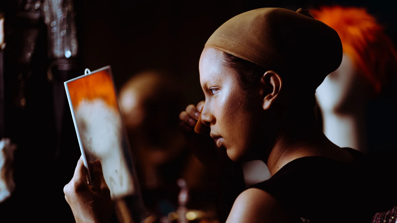 A woman holding a small mirror close to her face while applying make-up.