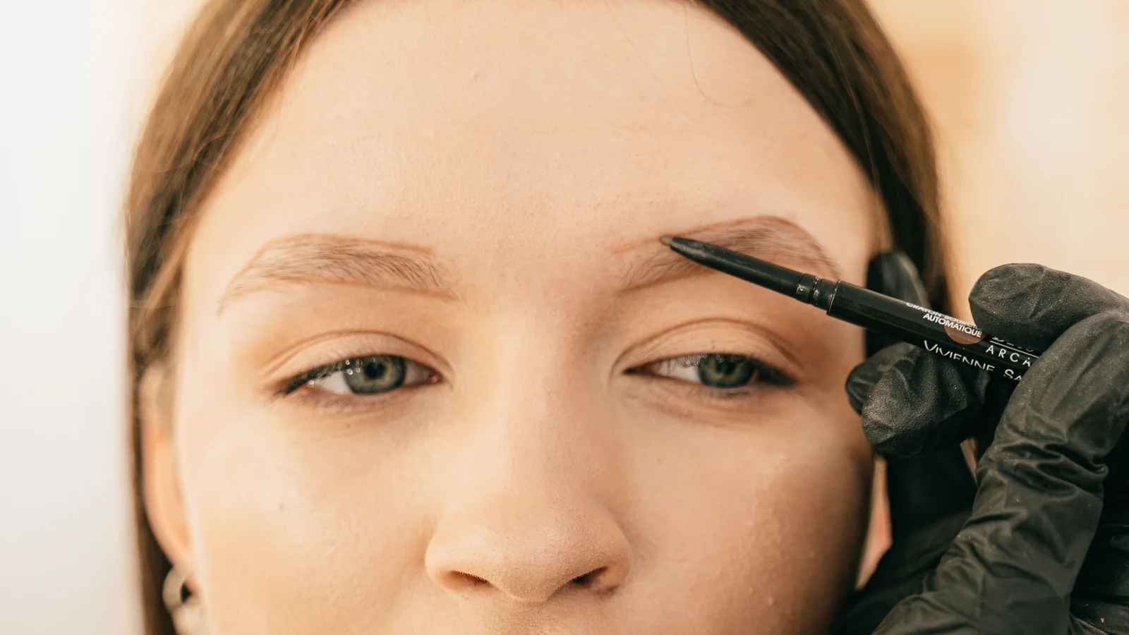 A practitioner brushing product along a woman's eyebrow.
