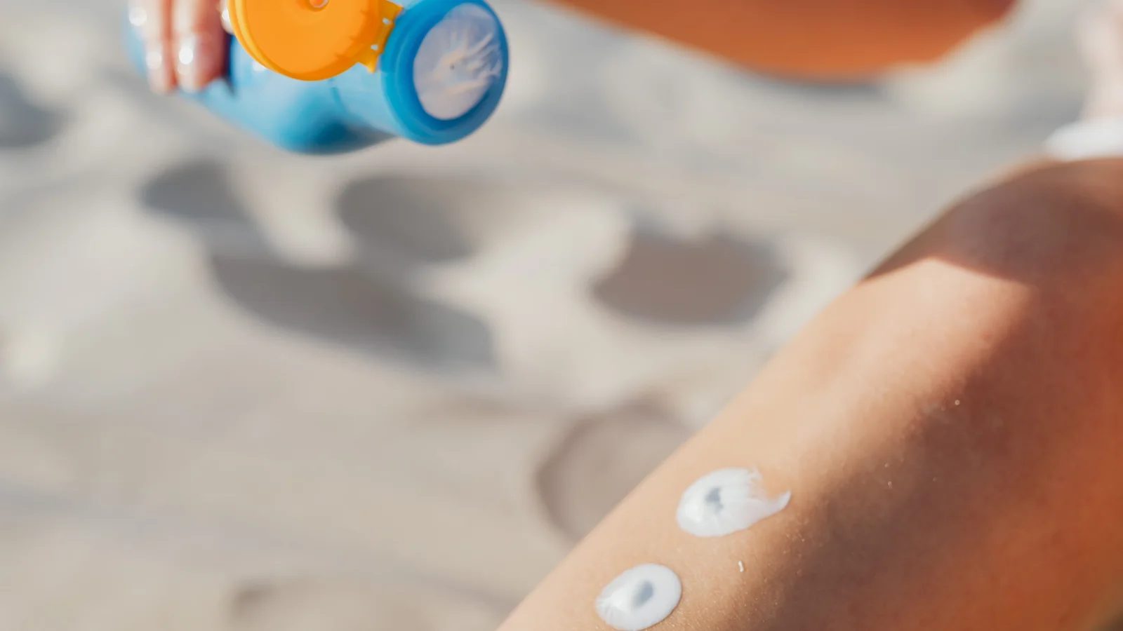 A woman placing small spots of lotion along her leg at a beach.