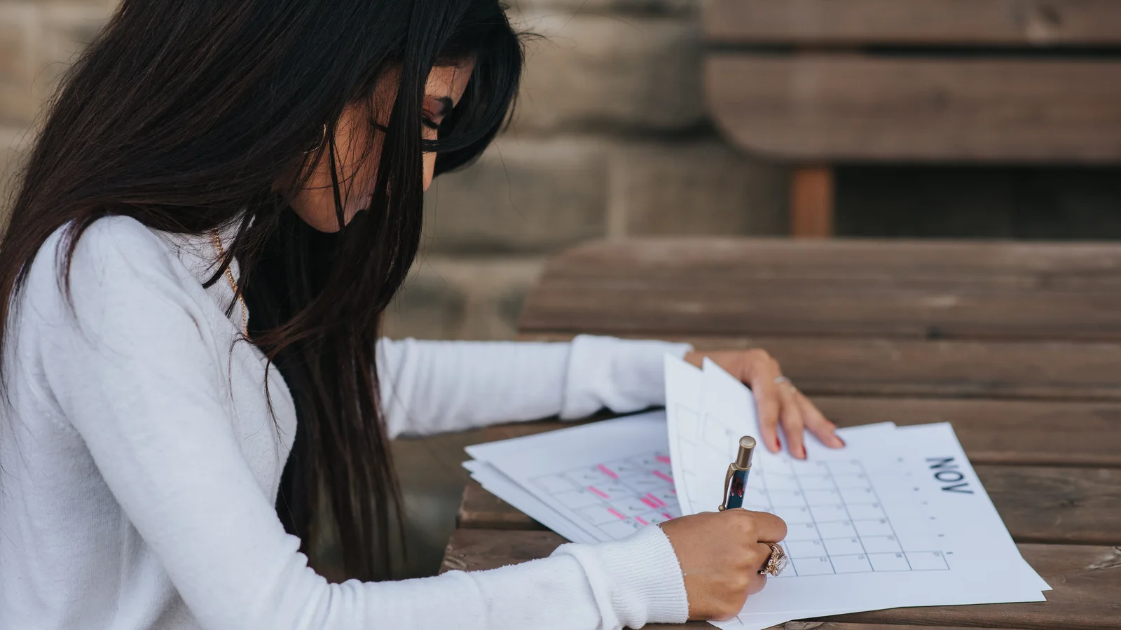 A woman writing on a calendar sheet beside a phone.