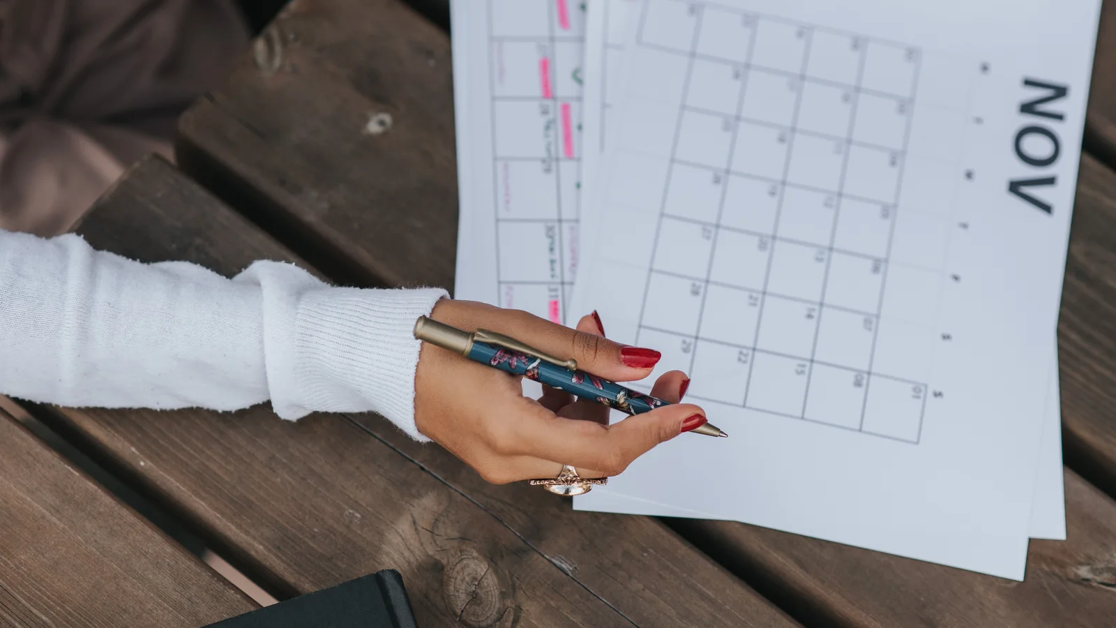 A hand holding pens above an open monthly calendar.