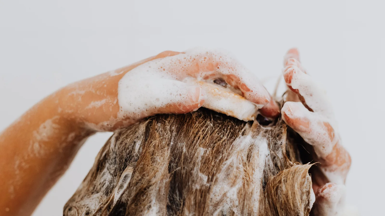 A person massaging foam through wet hair under a shower.
