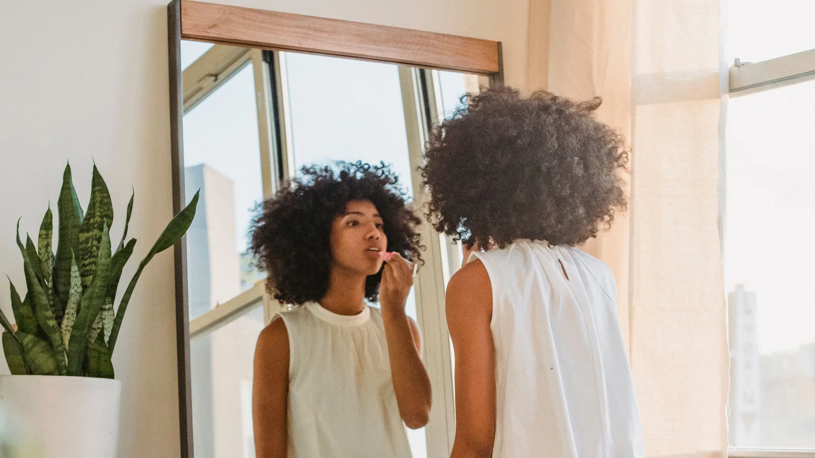 A woman checking her reflection in a full-length mirror with a small dog nearby.