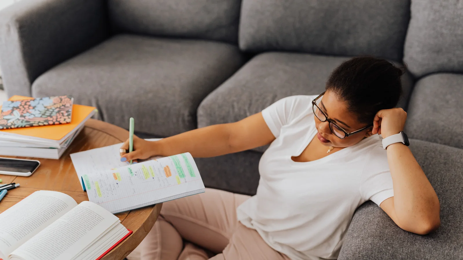 A woman reclining on a sofa with a notebook and pen.