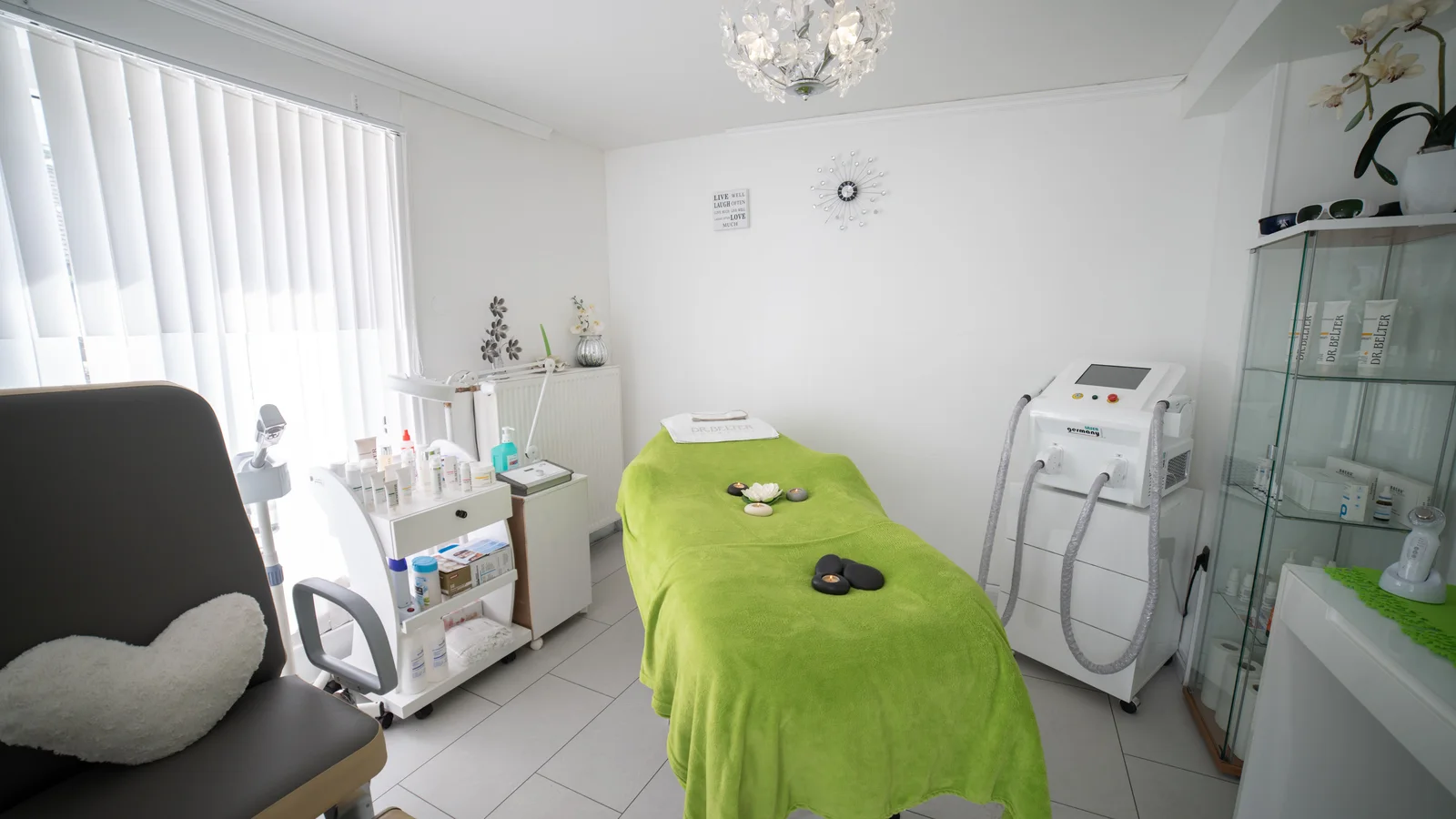 An empty treatment bed with a green cover in a bright treatment room.