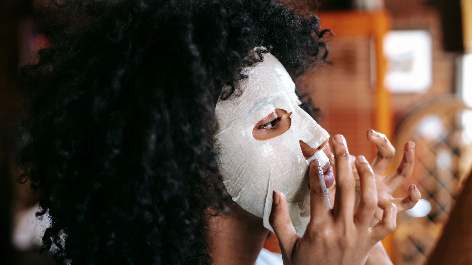 A woman pressing a white sheet mask onto her face.