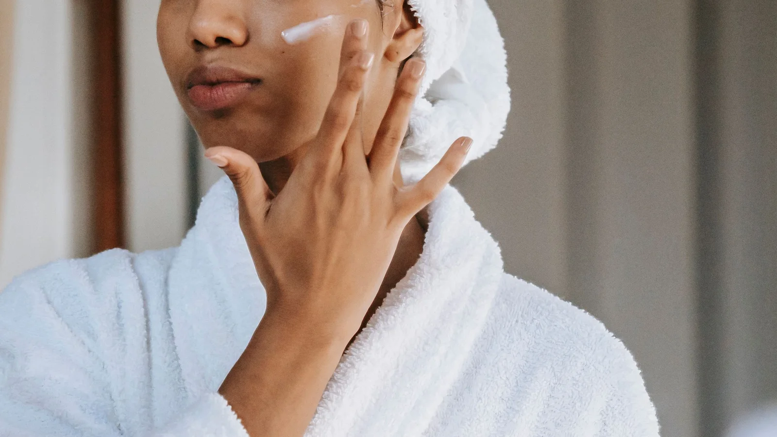 Close-up of a woman touching cream to her cheek while wearing a white robe.