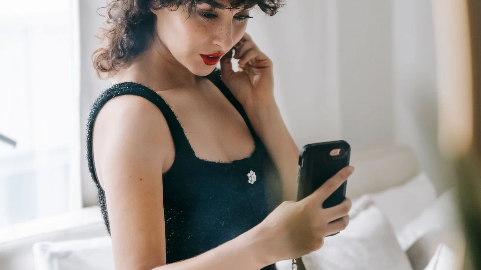 A woman holding a phone and touching her cheek beside a mirror.