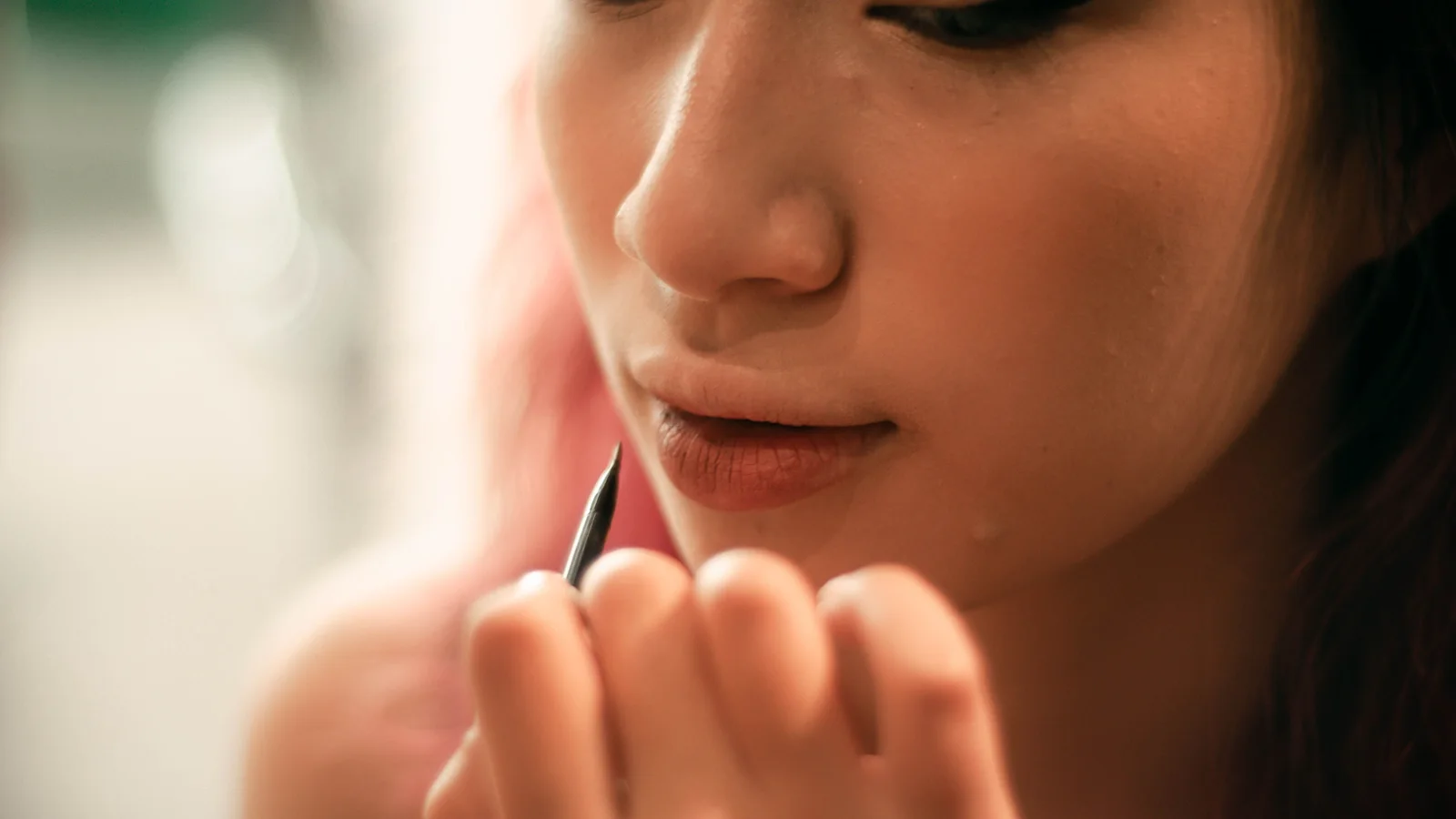 A woman tracing her lip with a cosmetic pencil.