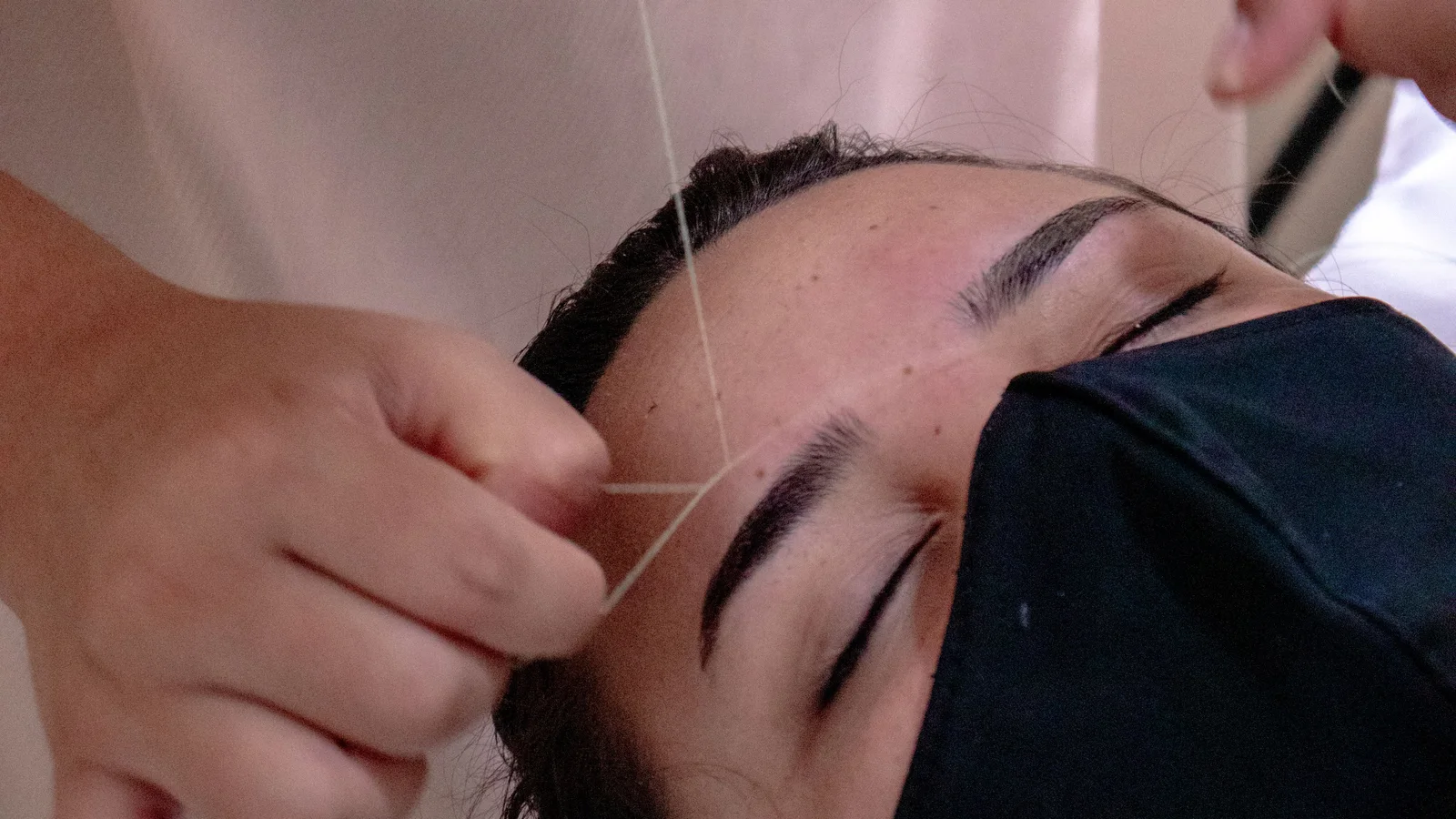 A practitioner removing hair around a woman's eyebrow with thread.