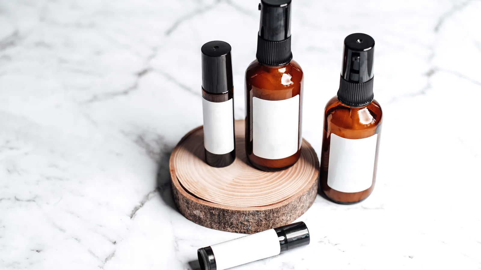 Amber cosmetic bottles with blank white labels on a round wooden slice.