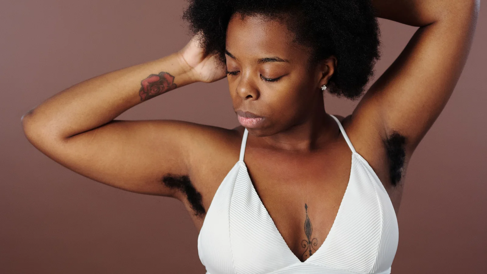 A woman with an afro and a white top standing with her arms raised behind her head.