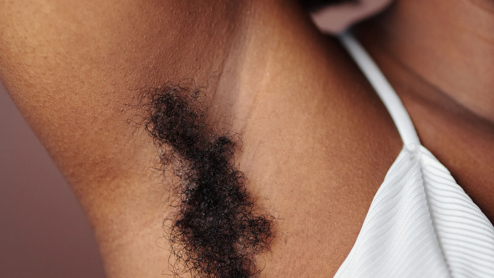 Close-up of an underarm with natural body hair beside a white shoulder strap.