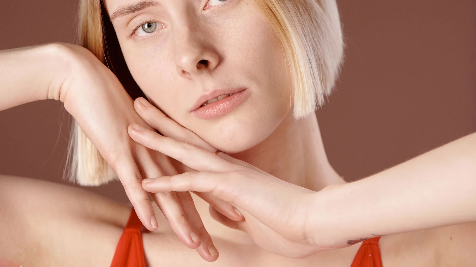 A woman in a red top resting her hands near her shoulder.