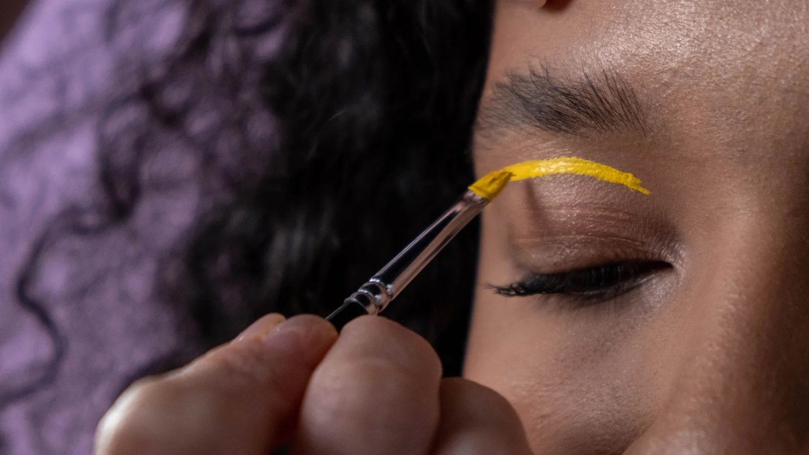 A make-up artist placing bright yellow colour on a woman's eyelid.